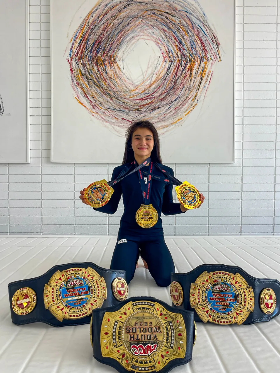 Bailey Heinsohn back at Art of Jiu Jitsu Academy with her championship belts and medals after winning double gold at the 2026 ADCC Youth World Championships.