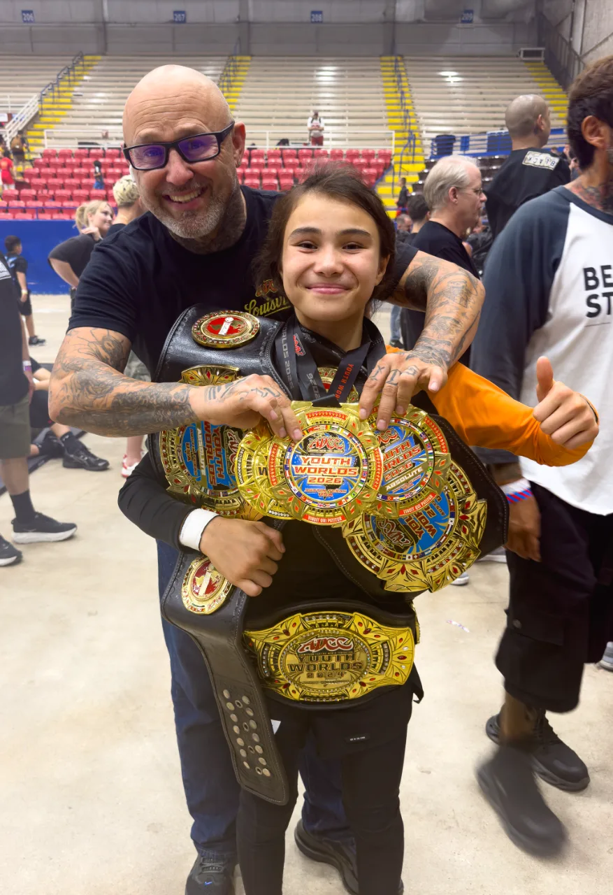 Bailey Heinsohn with ADCC’s Shawn Fowler, displaying her championship belts and medals after winning double gold at the 2026 ADCC Youth World Championships in Austin, Texas.