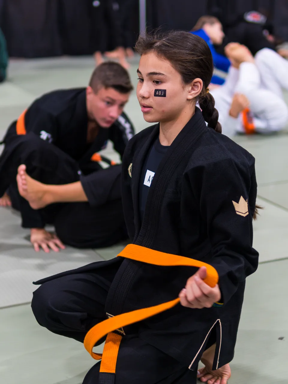 Bailey Heinsohn kneeling on the competition floor in her Gi and orange belt before competing at the 2026 IBJJF Jiu-Jitsu CON in Las Vegas.