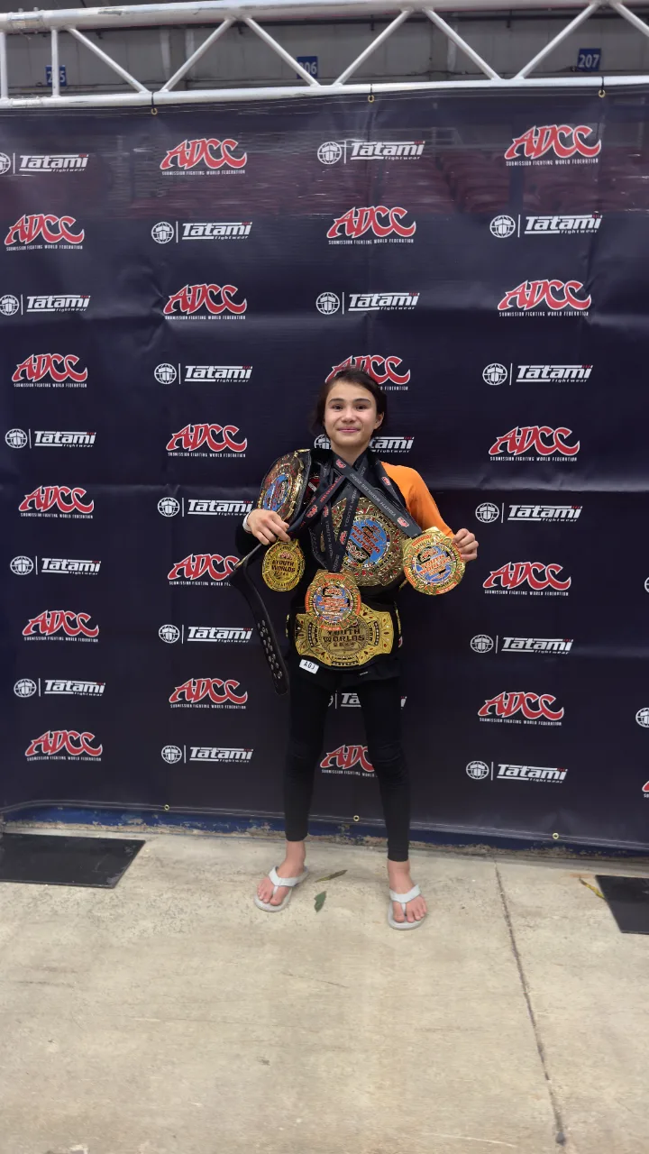 Bailey Heinsohn holding championship belts and medals after winning double gold at the 2026 ADCC Youth World Championships.